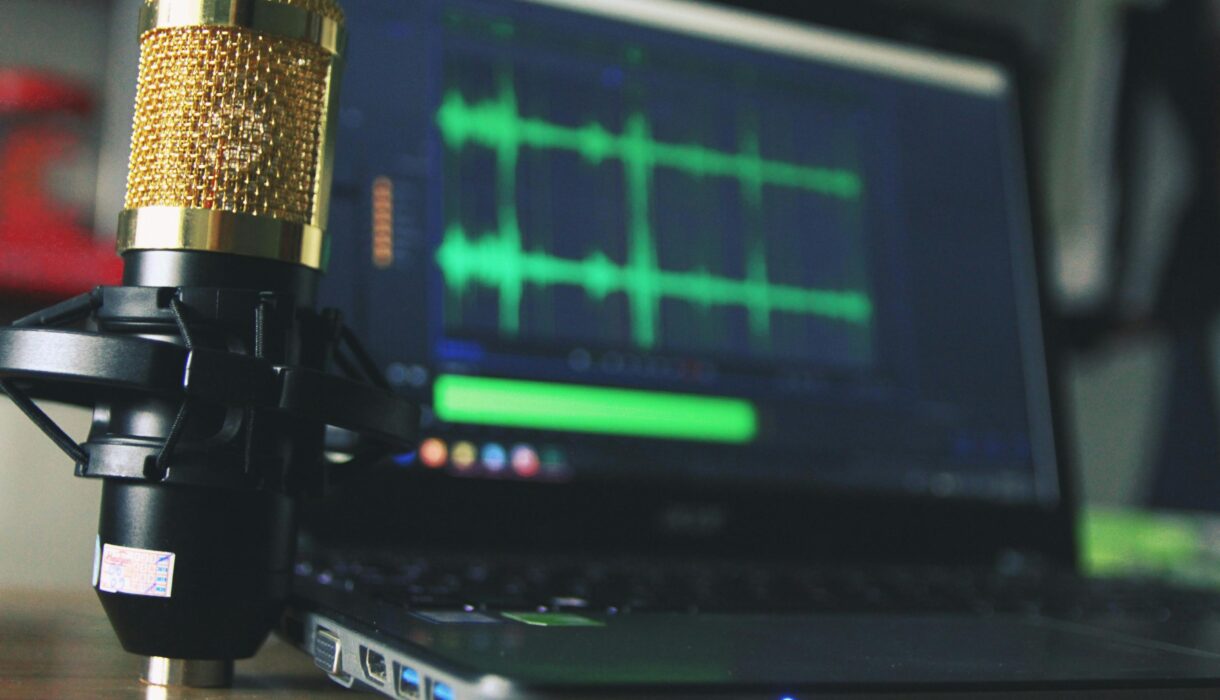 Close-up of a golden microphone and laptop used for audio editing.